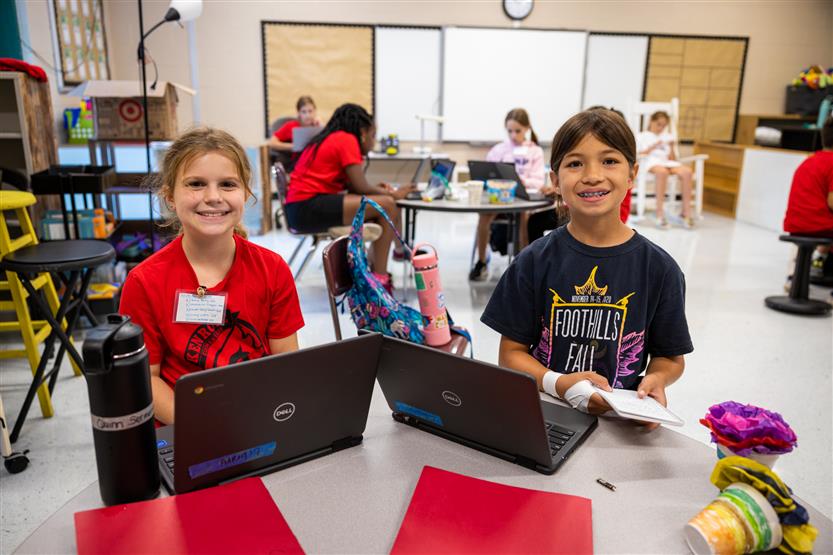 Two boys smile while using laptops